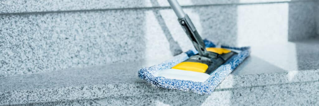 Mop bleue et jaune nettoyant des marches d'escalier en granit gris. Nettoyage professionnel des surfaces dures.